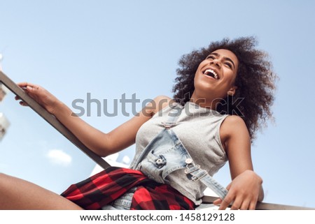 Young woman in the city standing on the balcony leaning on glass fence laughing cheerful bottom view
