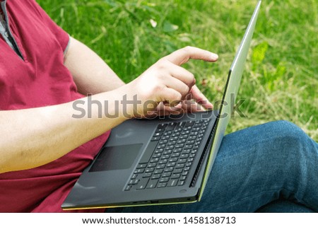 The man works on the computer. He sits in a chair and holds a laptop on his lap.