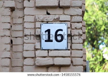 House number sixteen. Black lettering on a white metal plate on an old brick wall painted in white