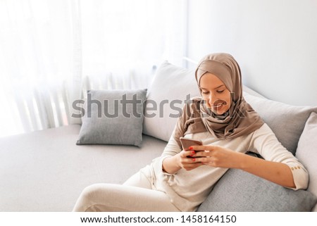 Portrait of happy muslim woman using mobile phone while sitting on a couch. Portrait of a muslim woman talking on the cell phone at home. Arab saudi emirates smiling woman using a smart phone