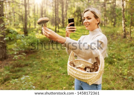 technology, people and leisure people concept - young woman with smartphone using app to identify mushroom in forest