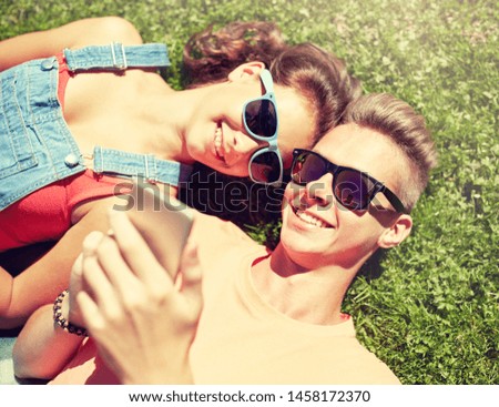 love and people concept - happy teenage couple in sunglasses with smartphone lying on grass at summer