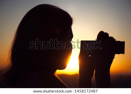 Silhouette of girl photographer taking picture on compact camera on the sunset background.