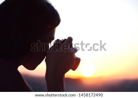 Silhouette of girl photographer taking picture setting sun on compact camera. sunset background.