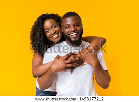 Pretty Black Girl Is Embracing Smiling Black Guy, portrait on yellow background Royalty-Free Stock Photo #1458177212