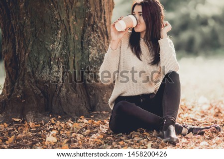 Beautiful woman drink coffee sitting in autumn park.