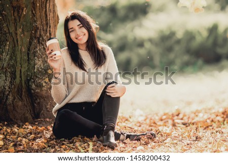 Beautiful woman drink coffee sitting in autumn park.