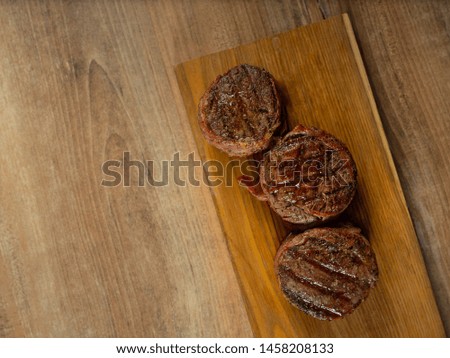 Cooked on grill beef steaks fillet mignon served on wooden plate on brown table with copy space for text menu. Top flat view, overhead.