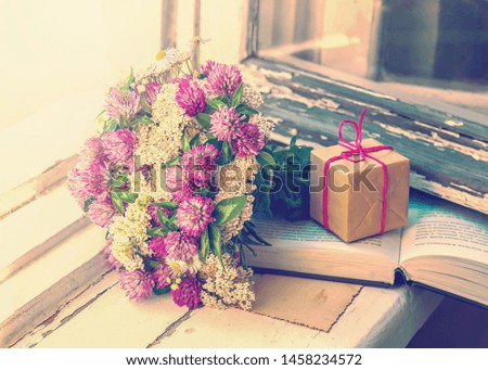 Bouquet of clover, a gift and a book on the window, toned.
