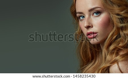 Beautiful young red-haired and fair-skinned girl with freckles posing in the studio on a gray background. Blue eyes.