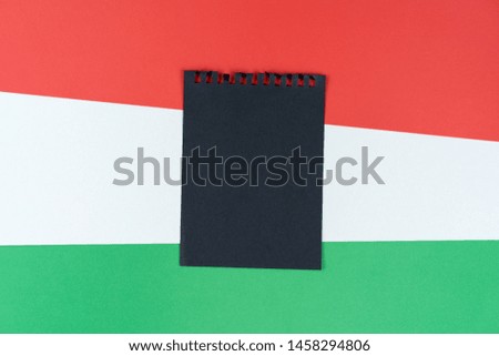 Blacklist Hungary. Mourning, ban, sanctions, politics. black sheet of notepad is on Hungarian flag. Mock up, copy space, pattern, cardboard texture.