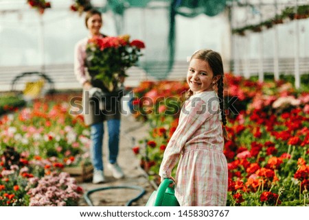 Cute little girl with watering can helping her mother at plant nursery. 