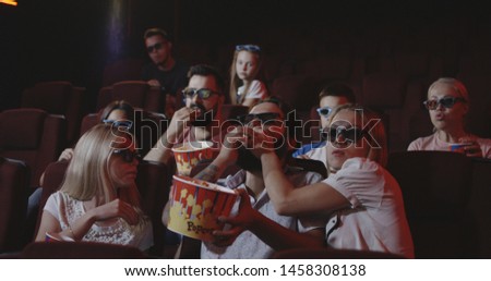 Medium shot of a young man spoiling movie for fellow moviegoers in cinema Royalty-Free Stock Photo #1458308138