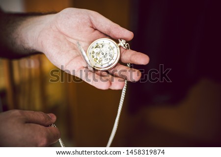 A man's hand holds an antique pocket watch with its gears and hand in sight.