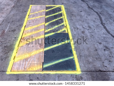 Rectangle manhole covered with temporary wooden boards with yellow spray painted diagonal lines to indicate a safety hazard