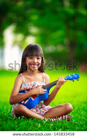 Little asian girl sitting on grass and play ukulele, Outdoor portrait