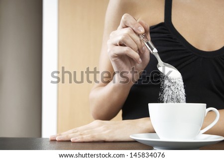 Closeup of a cropped woman pouring sugar into tea cup Royalty-Free Stock Photo #145834076