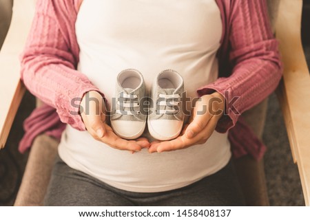 Pregnant woman feeling happy at home while taking care of her child. The young expecting mother holding baby in pregnant belly. Maternity prenatal care and woman pregnancy concept. Royalty-Free Stock Photo #1458408137