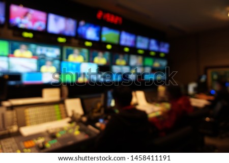 Blurred image of the TV production team in the broadcast control room, which includes video switch and audio mixer, control broadcasts in recording studio.
