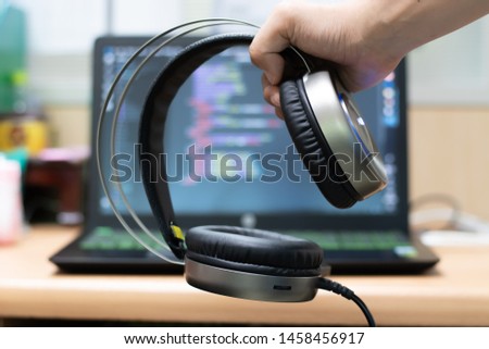 Hand holding headphone on laptop background.