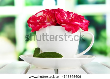 Roses in cup on table on window background