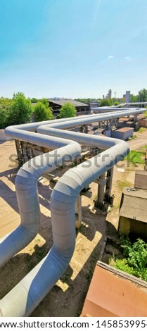 Industrial long pipeline with perspective, going into the distance of thick metal pipes on supports against blue sky. Vertical photo with copy space.