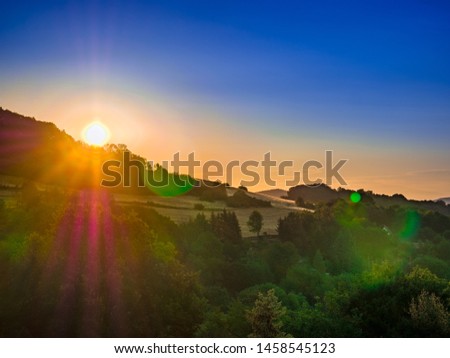 Golden sunrise over trees on the horizon of the hill with strong colorful flares and blue sky