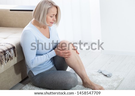 Middle-aged woman suffering from pain in leg at home, closeup. Physical injury concept. Ankle pain, painful point. Royalty-Free Stock Photo #1458547709