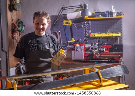 A man in work clothes repairman in the workshop ski service repairing the ski