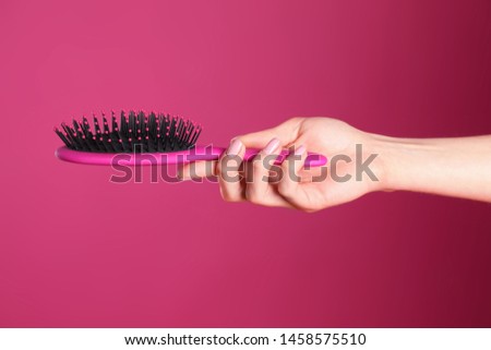 Woman holding hair brush against crimson background, closeup
