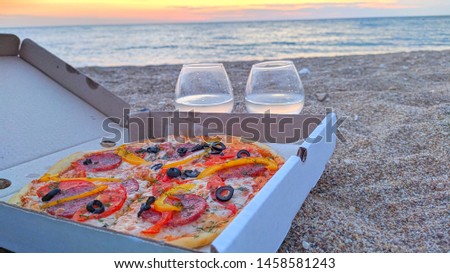 Closeup of box with delicious pizza with chease and salami with wineglass over view on ocean and sunset Royalty-Free Stock Photo #1458581243