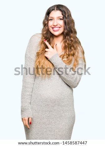 Young beautiful woman wearing winter dress cheerful with a smile of face pointing with hand and finger up to the side with happy and natural expression on face
