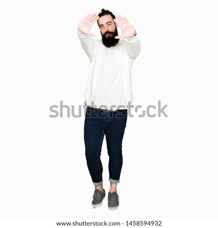 Young hipster man with long hair and beard wearing sporty sweatshirt Smiling doing frame using hands palms and fingers, camera perspective