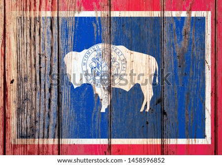 Wyoming US state national flag on a gray wooden boards background on the day of independence in different colors of blue red and yellow. Political and religious disputes, customs and delivery.