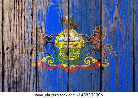 Pennsylvania US state national flag on a gray wooden boards background on the day of independence in different colors of blue red and yellow. Political and religious disputes, customs and delivery.