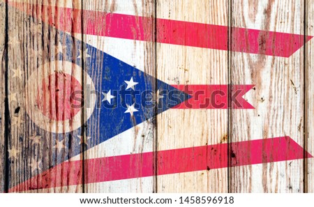 Ohio US state national flag on a gray wooden boards background on the day of independence in different colors of blue red and yellow. Political and religious disputes, customs and delivery.