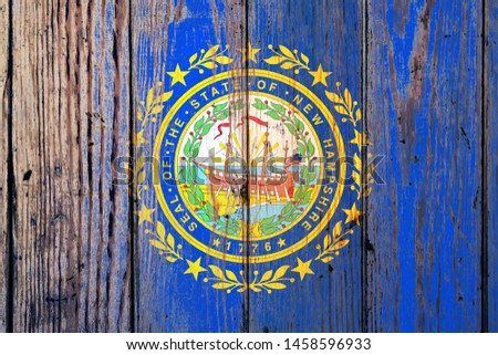 New Hampshire US state national flag on a gray wooden boards background on the day of independence in different colors of blue red and yellow. Political and religious disputes, customs and delivery.