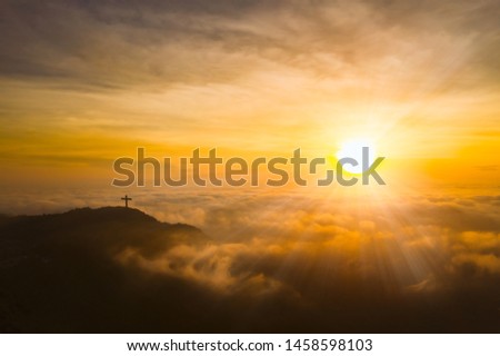Beautiful golden sunrise sky above fluffy cloudy with Christianity crucifix on mountain peak, dramatic light in twilight sky. Aerial view from drone.