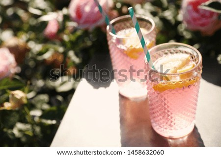 Glasses of pink rose lemonade on  table in blooming garden. Space for text