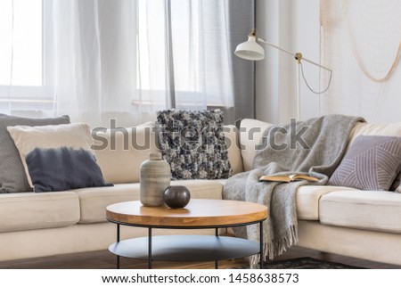 Round wooden coffee table in front of scandinavian corner sofa with pillows Royalty-Free Stock Photo #1458638573