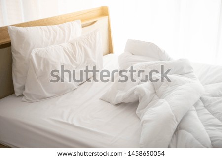 White unmade bed in the morning with sunshine with white curtain background in elegant home. Interior design and luxury furniture concept. Indoors lifestyle and Lazy activity theme.