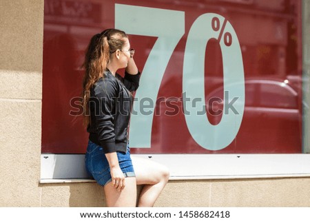 Fashionable woman looking at 70 percentage sale marketing sign. Female wants to buy something at shop.