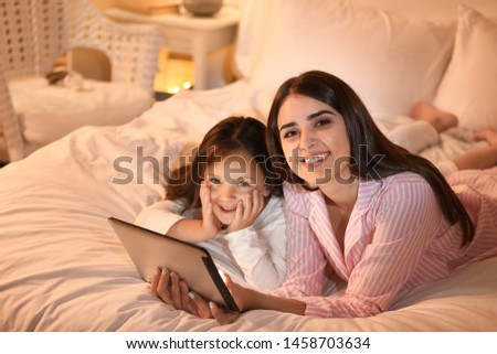 Woman and her cute little daughter with tablet computer in bedroom