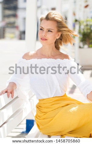 Beautiful young blond model in white top, sitting on bench Royalty-Free Stock Photo #1458705860