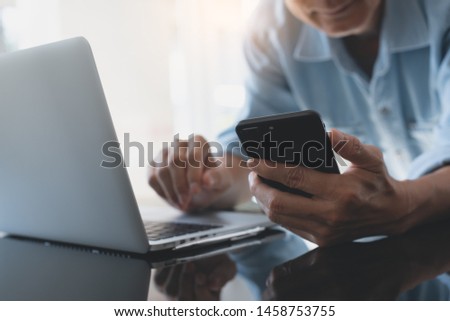 Casual business man, freelancer working and browsing internet on laptop computer in office with mobile smart phone on desk with reflection and copy space, close up. Online working, e-business concept