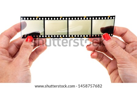 female hand with red nails holding long 35mm film strip with empty frames or film cells, just blend in your photos here via blend mode, hands holding something Royalty-Free Stock Photo #1458757682