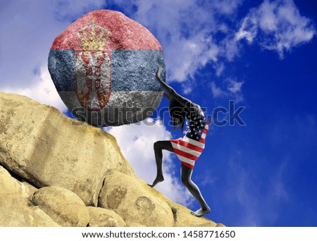 The girl, wrapped in the flag of the United States of America, raises a stone to the top in the form of a Serbian flag