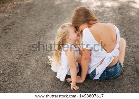 Attractive Mom and blonde hair daughter sits on road near big alley. They smile and look to natune. Back view