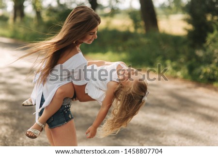 little girl playing with mom in the park in summer day during the sunset spin around