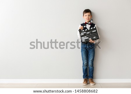 Little boy with clapperboard near white wall